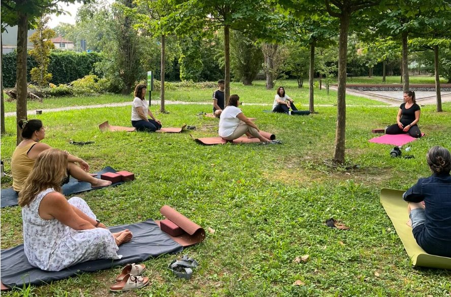 Grupo sentado sobre mats en el césped de un parque durante una sesión de meditación activa en Boloña